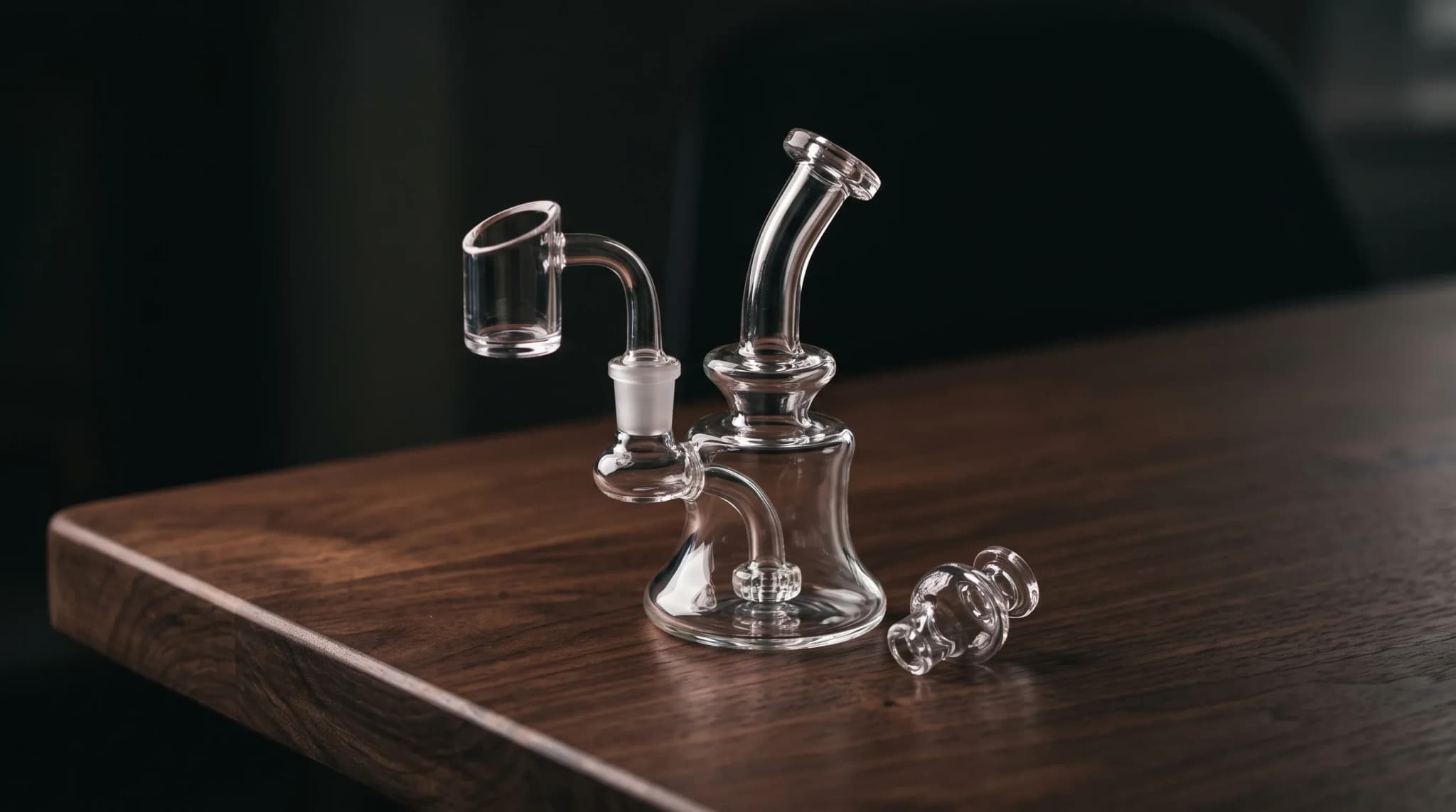 A small clear glass dab rig with a quartz banger on a dark wooden table