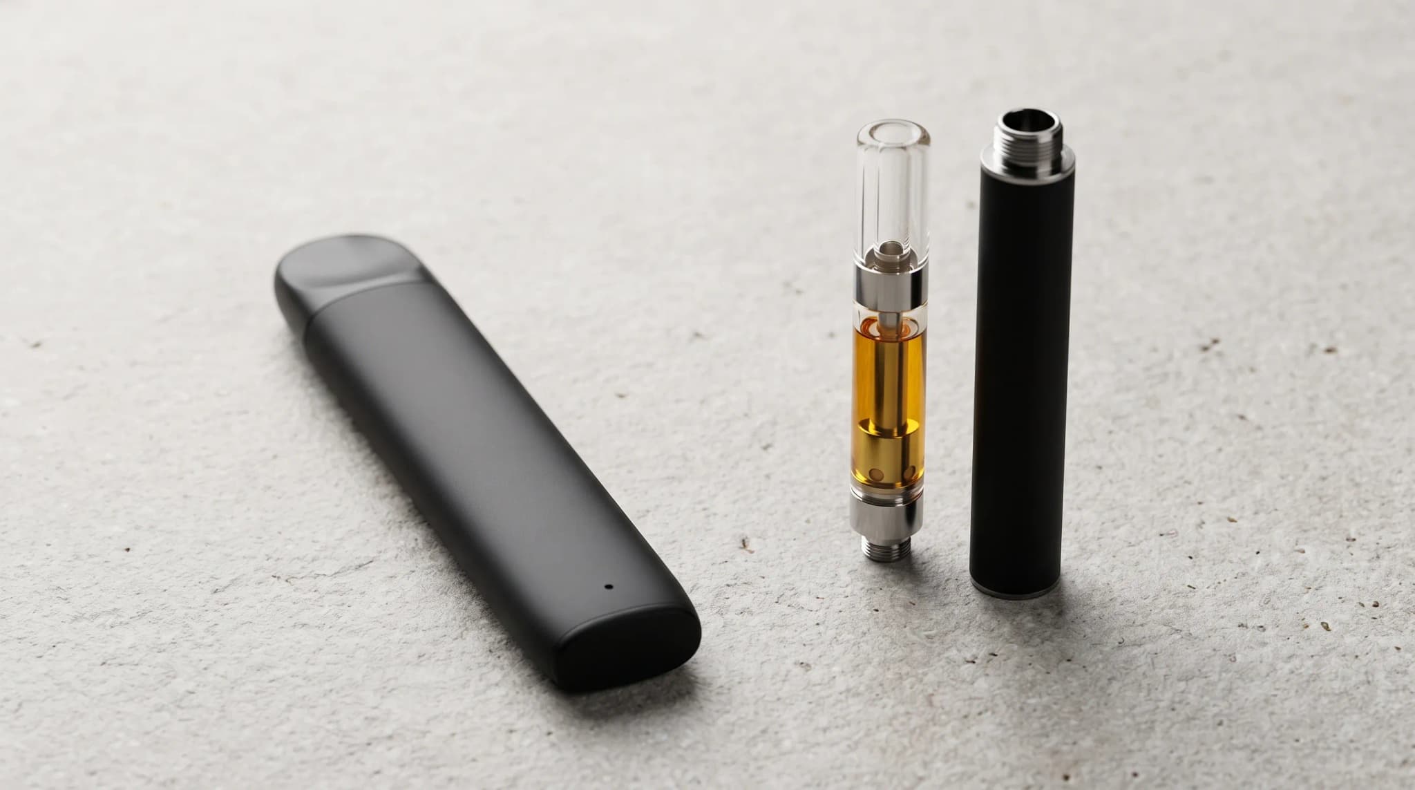 A slim all-in-one vape beside a cartridge and a separate pen battery on a light stone surface