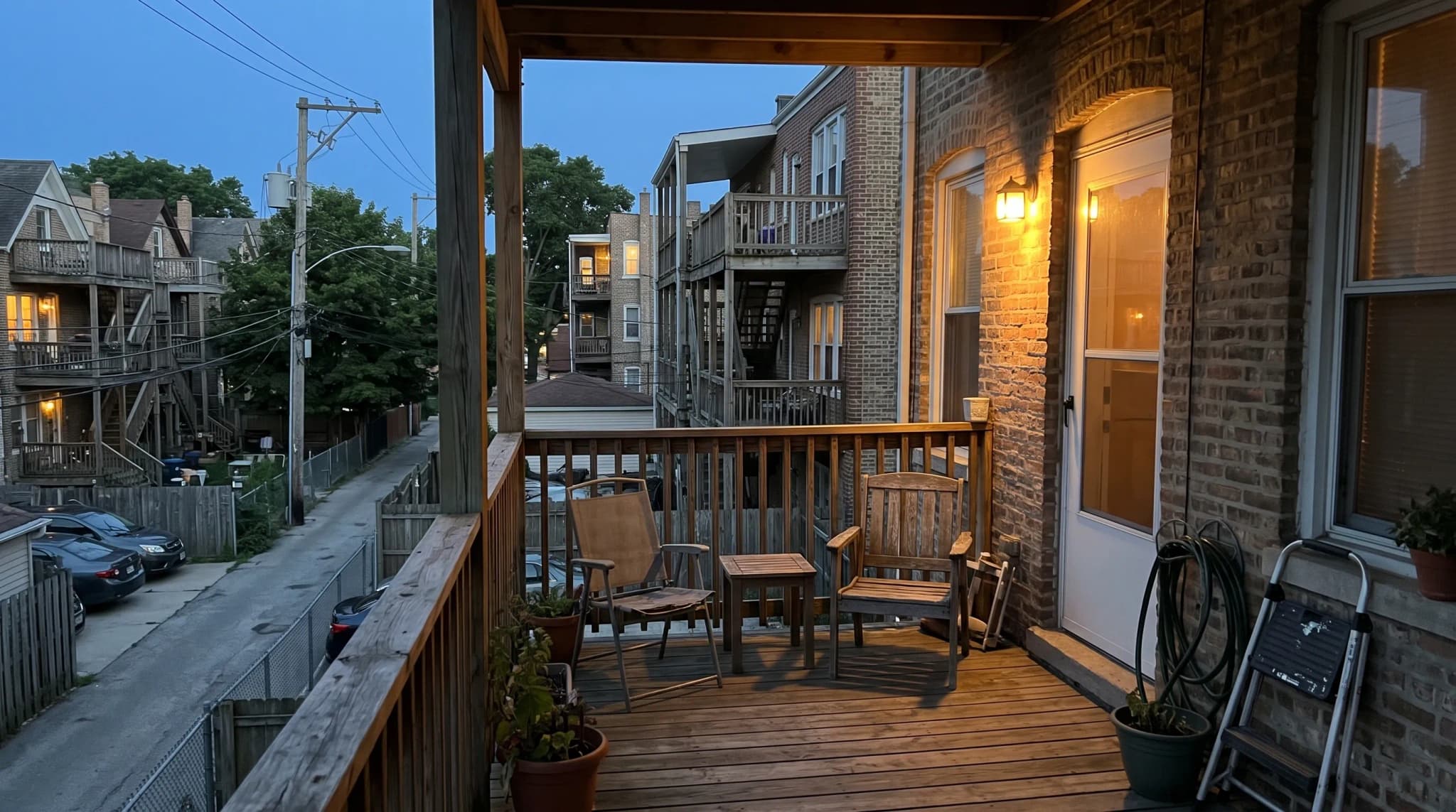 A covered back porch on a brick Chicago building overlooking an alley and neighboring rear porches at dusk
